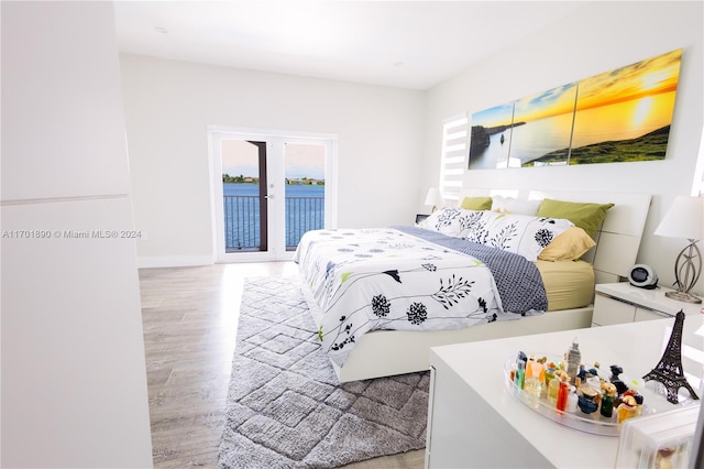 bedroom featuring a water view, french doors, access to outside, and light hardwood / wood-style flooring