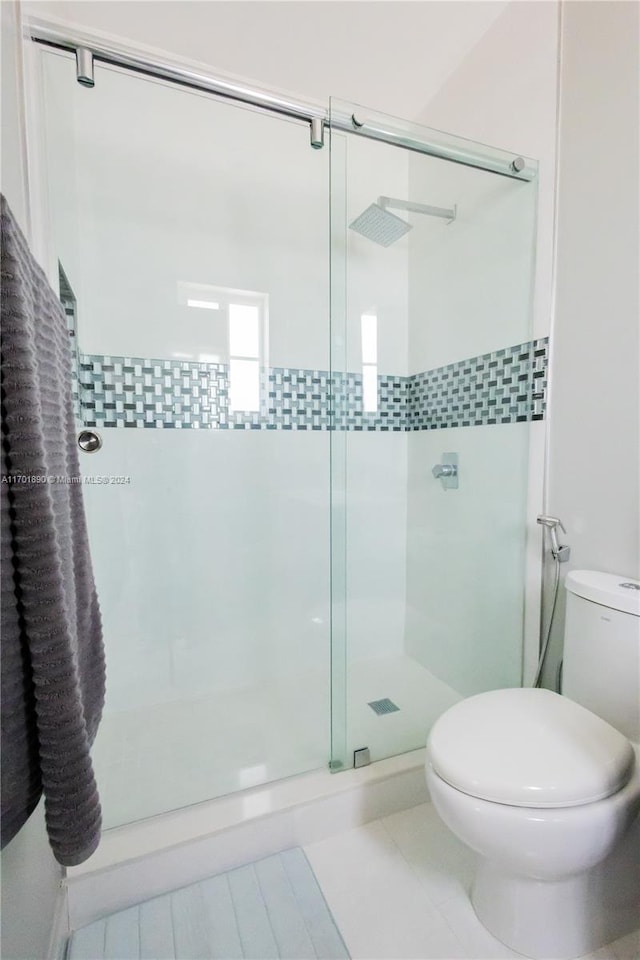 bathroom featuring tile patterned flooring, toilet, and an enclosed shower