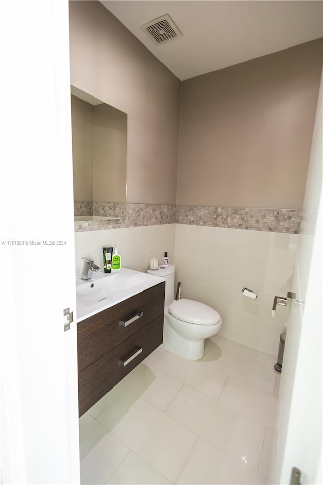 bathroom with toilet, vanity, tile patterned floors, and tile walls