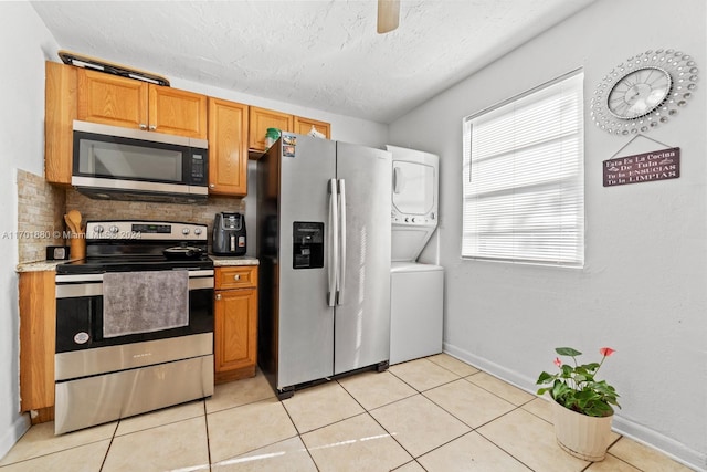 kitchen featuring stacked washer and clothes dryer, light tile patterned floors, a textured ceiling, tasteful backsplash, and stainless steel appliances