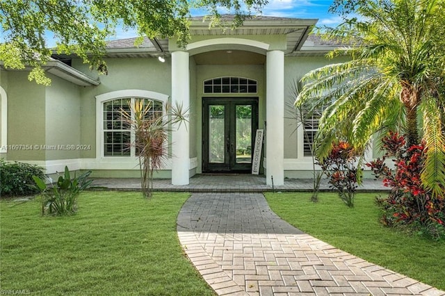 view of exterior entry with a lawn and french doors