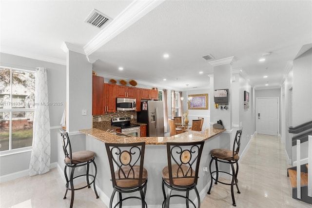 kitchen featuring light stone counters, appliances with stainless steel finishes, a kitchen bar, and kitchen peninsula