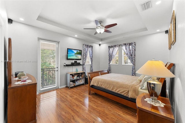 bedroom with a raised ceiling, hardwood / wood-style flooring, access to outside, and multiple windows