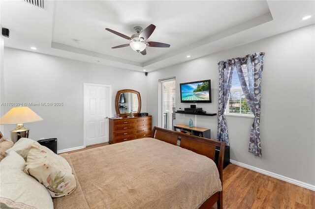 bedroom with ceiling fan, wood-type flooring, and a tray ceiling