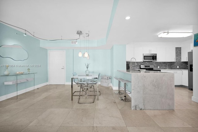 kitchen with stainless steel appliances, backsplash, decorative light fixtures, a breakfast bar area, and white cabinets