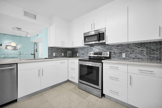 kitchen featuring pendant lighting, sink, appliances with stainless steel finishes, tasteful backsplash, and white cabinetry