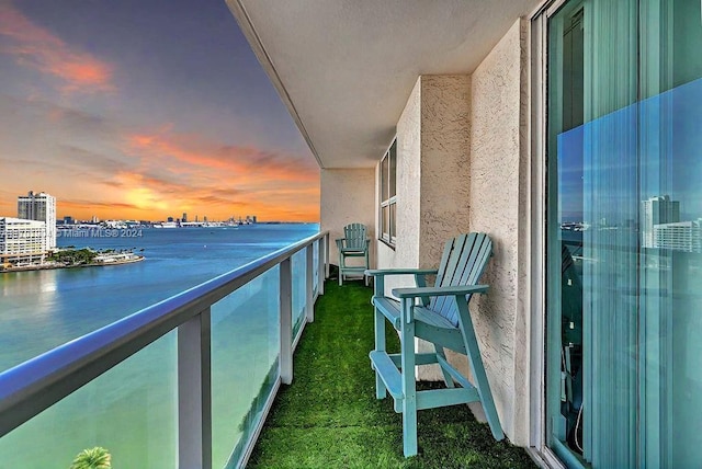 balcony at dusk featuring a water view