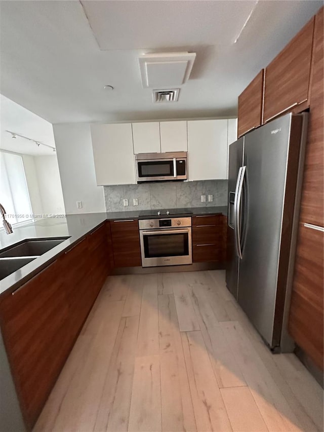 kitchen with white cabinetry, sink, stainless steel appliances, tasteful backsplash, and light wood-type flooring