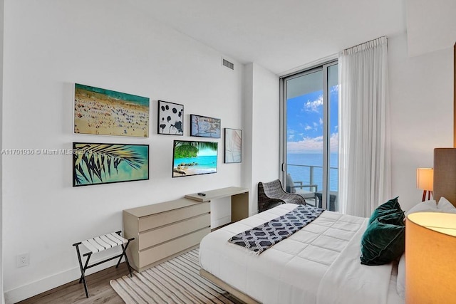 bedroom featuring expansive windows, light hardwood / wood-style floors, a water view, and access to outside