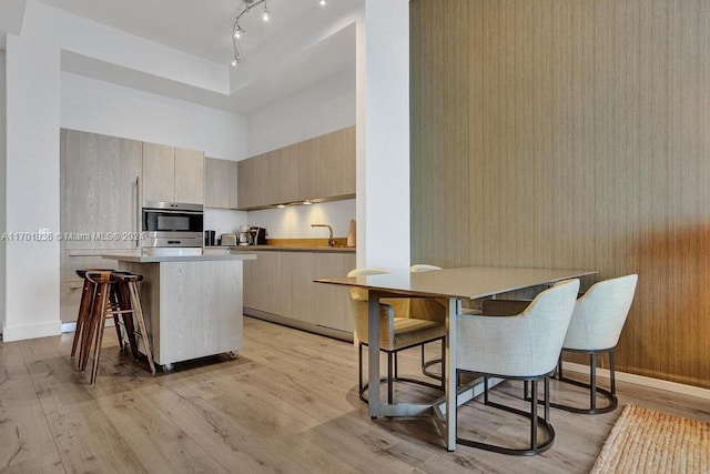 kitchen with a center island, light brown cabinets, a kitchen breakfast bar, light hardwood / wood-style flooring, and oven