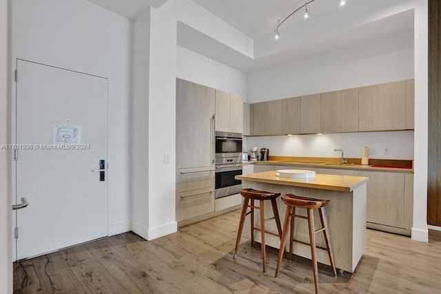 kitchen featuring a breakfast bar, stainless steel double oven, sink, light hardwood / wood-style floors, and a kitchen island