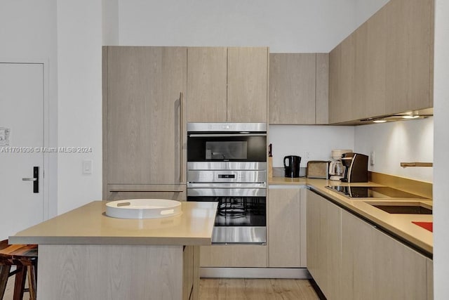 kitchen featuring double oven, light hardwood / wood-style floors, a kitchen bar, and light brown cabinetry