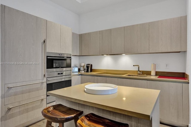 kitchen with a kitchen bar, light brown cabinets, stainless steel double oven, and sink