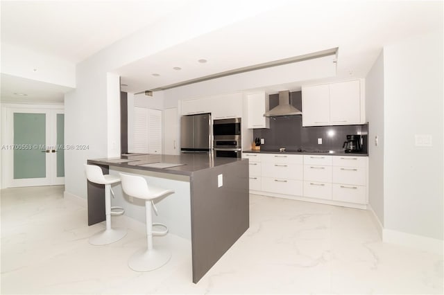 kitchen with kitchen peninsula, appliances with stainless steel finishes, white cabinetry, and wall chimney exhaust hood