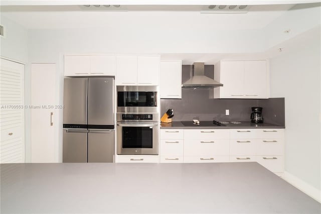 kitchen with decorative backsplash, white cabinets, wall chimney range hood, and appliances with stainless steel finishes