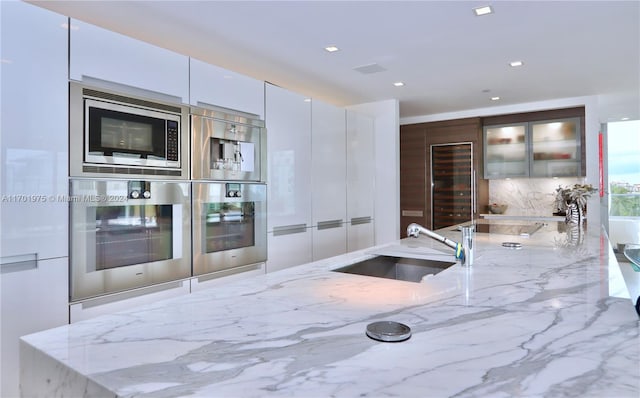 kitchen featuring light stone countertops, stainless steel appliances, white cabinets, and sink