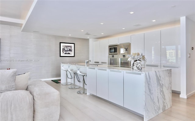 kitchen featuring a large island with sink, stainless steel microwave, white cabinets, and light wood-type flooring