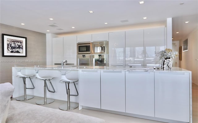 kitchen with white cabinetry, sink, stainless steel appliances, light stone counters, and a kitchen bar