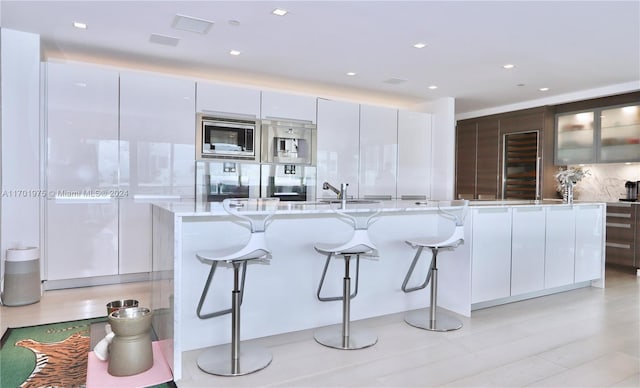 kitchen featuring white cabinetry, stainless steel microwave, a center island, decorative backsplash, and a breakfast bar