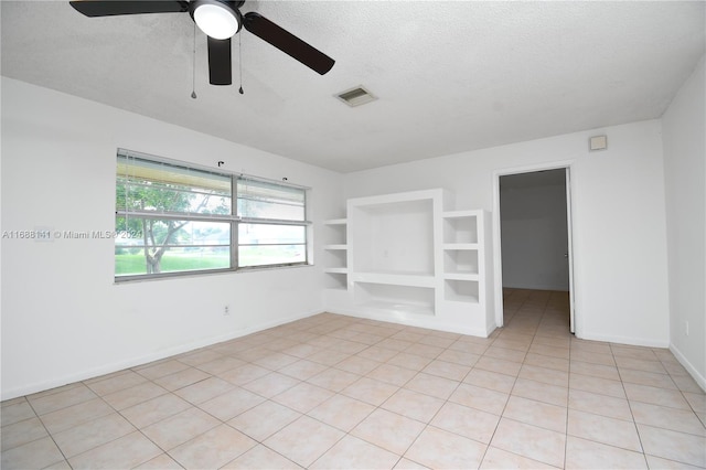 spare room with ceiling fan, built in features, light tile patterned floors, and a textured ceiling