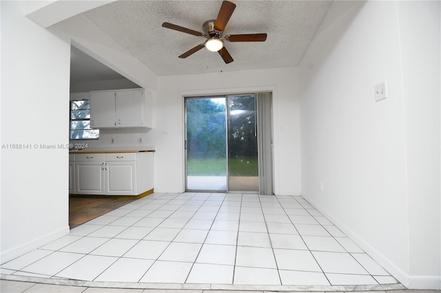 interior space with white cabinets, a textured ceiling, ceiling fan, and light tile patterned flooring