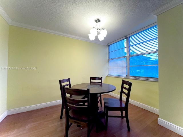 dining space with wood-type flooring, a textured ceiling, ornamental molding, and a notable chandelier