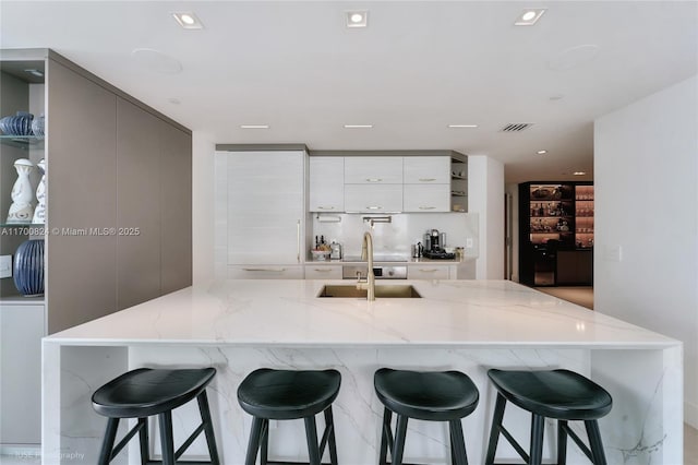 kitchen with light stone counters, open shelves, visible vents, modern cabinets, and a sink