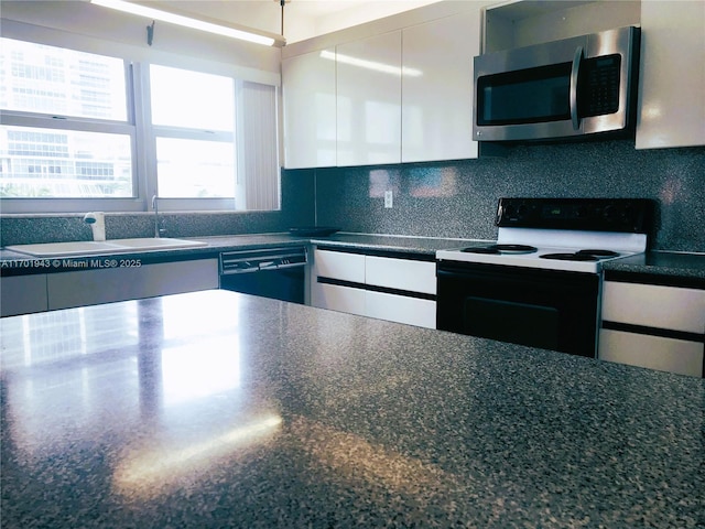 kitchen with electric range oven, stainless steel microwave, dishwashing machine, and white cabinetry
