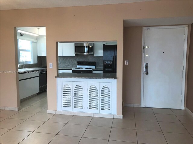 kitchen with light tile patterned floors, backsplash, white cabinetry, and black appliances