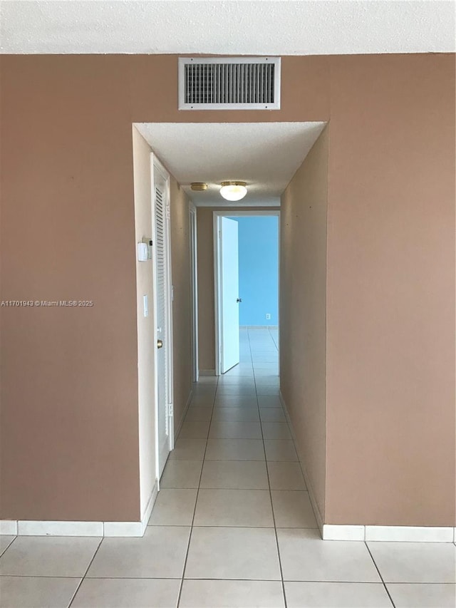 hall with a textured ceiling, baseboards, visible vents, and light tile patterned floors