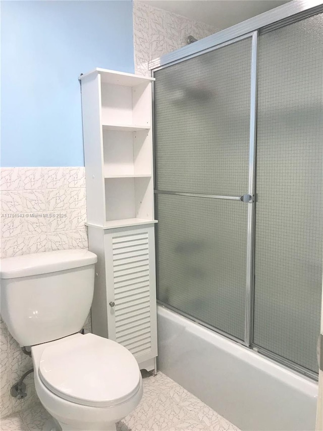 bathroom featuring bath / shower combo with glass door, toilet, tile walls, and marble finish floor