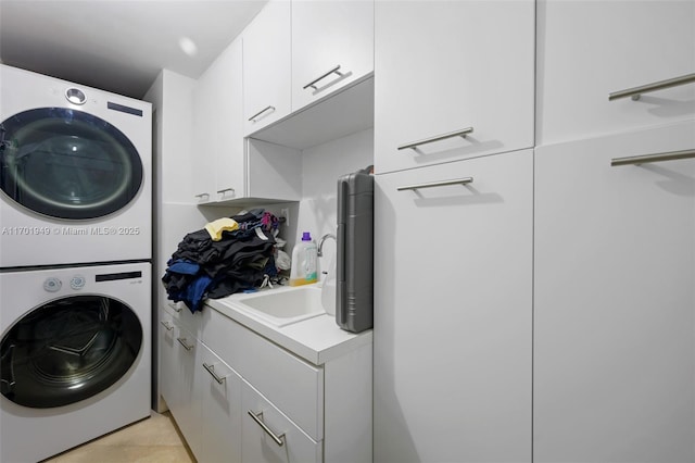 clothes washing area with stacked washer and dryer, light tile patterned floors, and cabinets