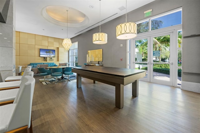 game room featuring a tray ceiling, french doors, a notable chandelier, and hardwood / wood-style flooring