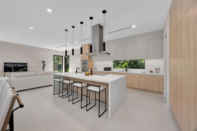 kitchen with a breakfast bar, pendant lighting, white cabinetry, exhaust hood, and a center island with sink