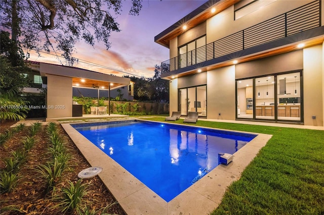 pool at dusk featuring a patio area and a lawn