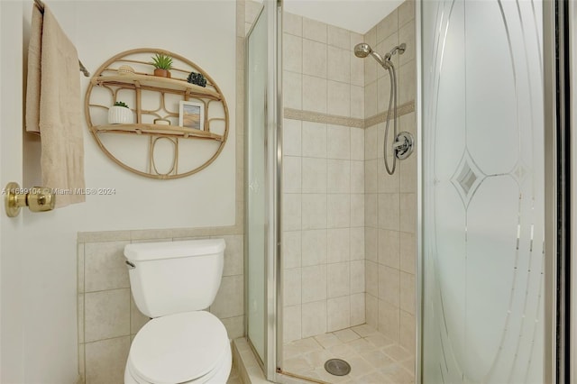 bathroom featuring toilet, a shower with door, and tile walls