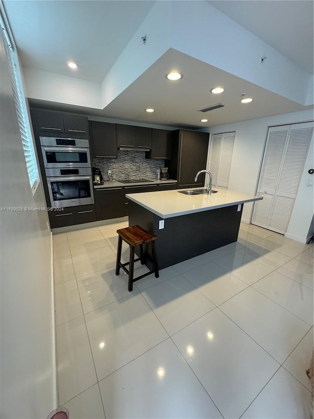 kitchen featuring a kitchen bar, black electric stovetop, decorative backsplash, sink, and a center island with sink