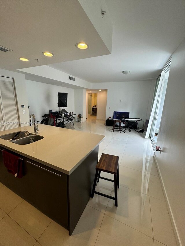 kitchen with a breakfast bar, light tile patterned floors, dark brown cabinets, and sink