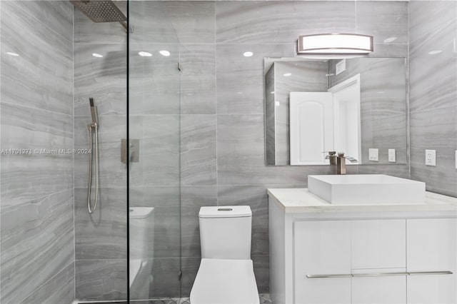 bathroom with tiled shower, vanity, toilet, and tile walls