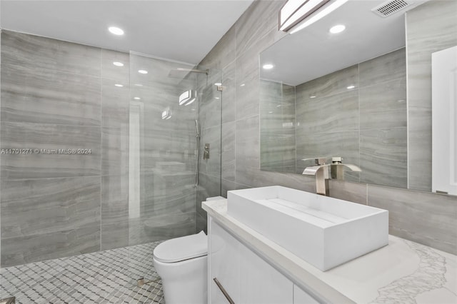 bathroom featuring vanity, toilet, tile walls, and a tile shower