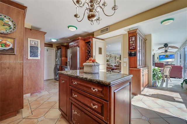 kitchen with hanging light fixtures, stainless steel fridge, stacked washer / drying machine, a kitchen island, and ceiling fan with notable chandelier