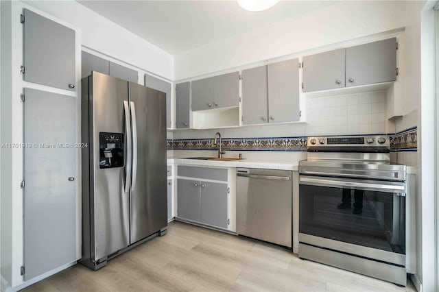 kitchen featuring backsplash, sink, gray cabinets, light wood-type flooring, and stainless steel appliances