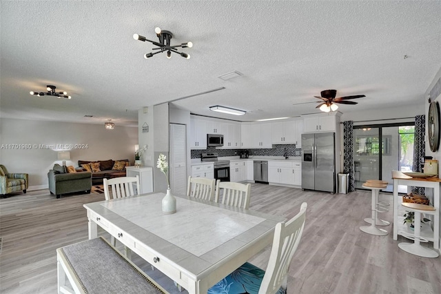 dining space featuring ceiling fan with notable chandelier, a textured ceiling, and light wood-type flooring