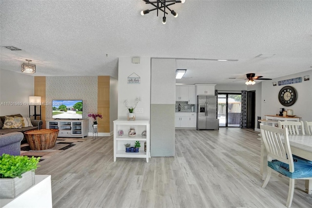 living room featuring ceiling fan with notable chandelier, light hardwood / wood-style floors, and a textured ceiling