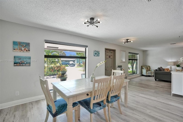 dining room with light wood-type flooring, a textured ceiling, and a wealth of natural light