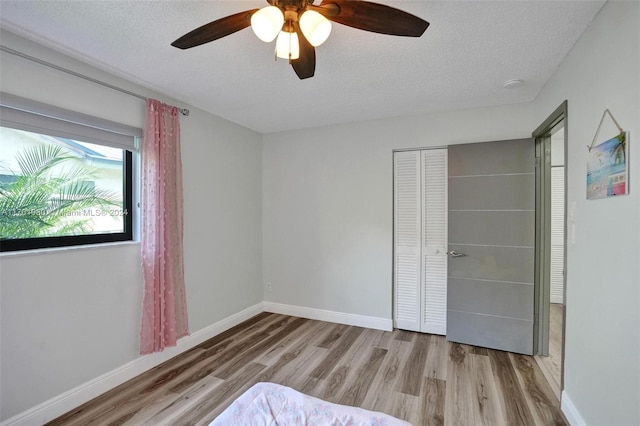 unfurnished bedroom with a textured ceiling, light wood-type flooring, a closet, and ceiling fan