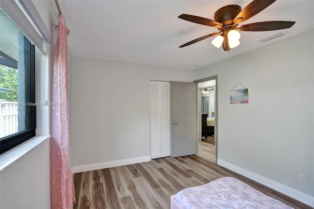 unfurnished bedroom featuring ceiling fan, a closet, light hardwood / wood-style floors, and a textured ceiling