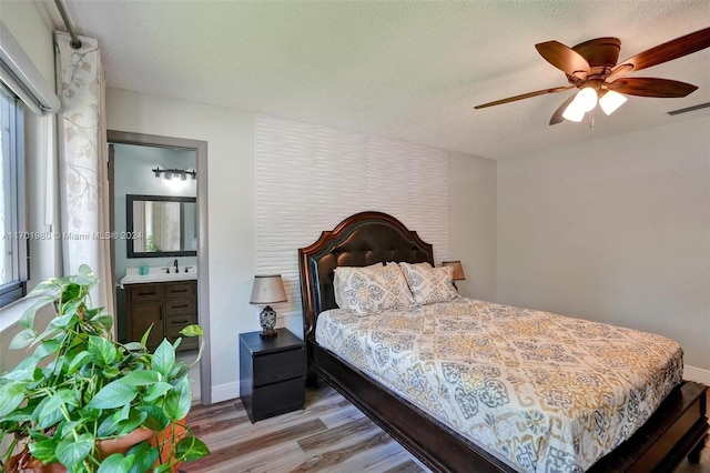 bedroom with a textured ceiling, ensuite bathroom, ceiling fan, and light hardwood / wood-style floors