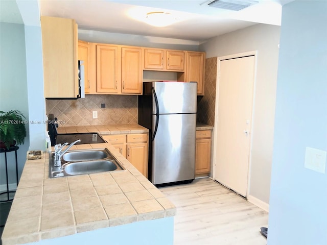 kitchen with stainless steel fridge, light wood-type flooring, backsplash, and light brown cabinets