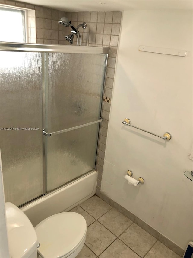 bathroom featuring tile patterned flooring, bath / shower combo with glass door, and toilet